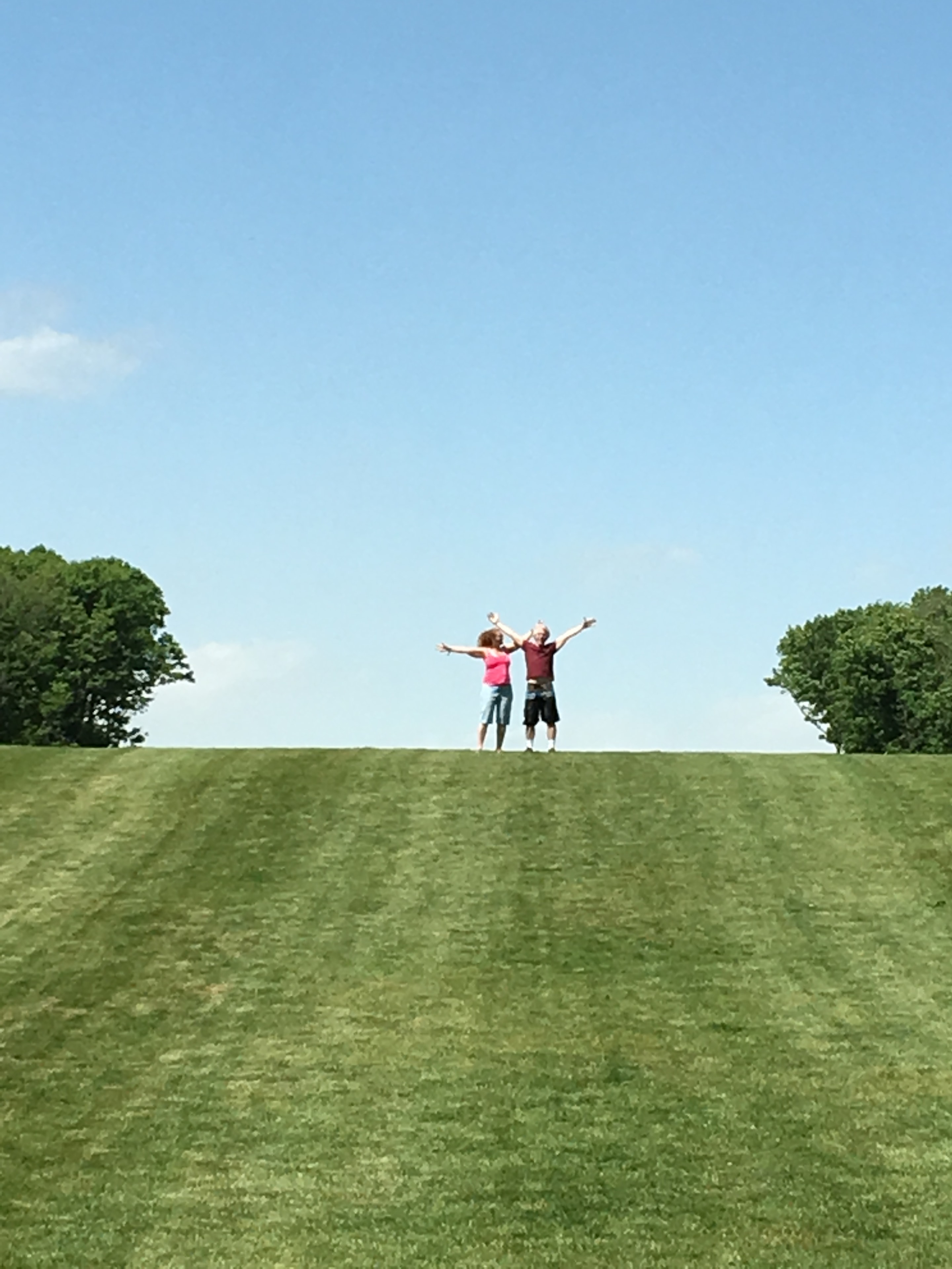 Two people in a sunny green field with arms raised
