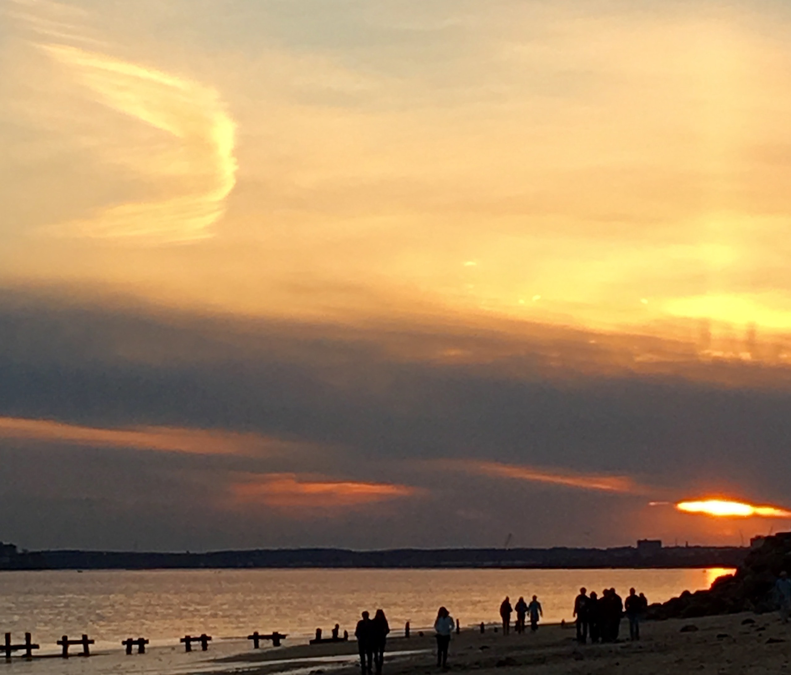 Sunset over the water with silhouetted people on the beach